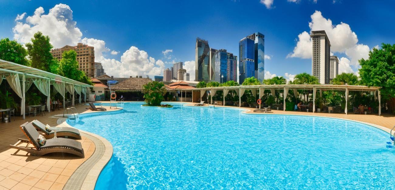Hotelpool mit Sonnenliegen vor einer Stadtsilhouette