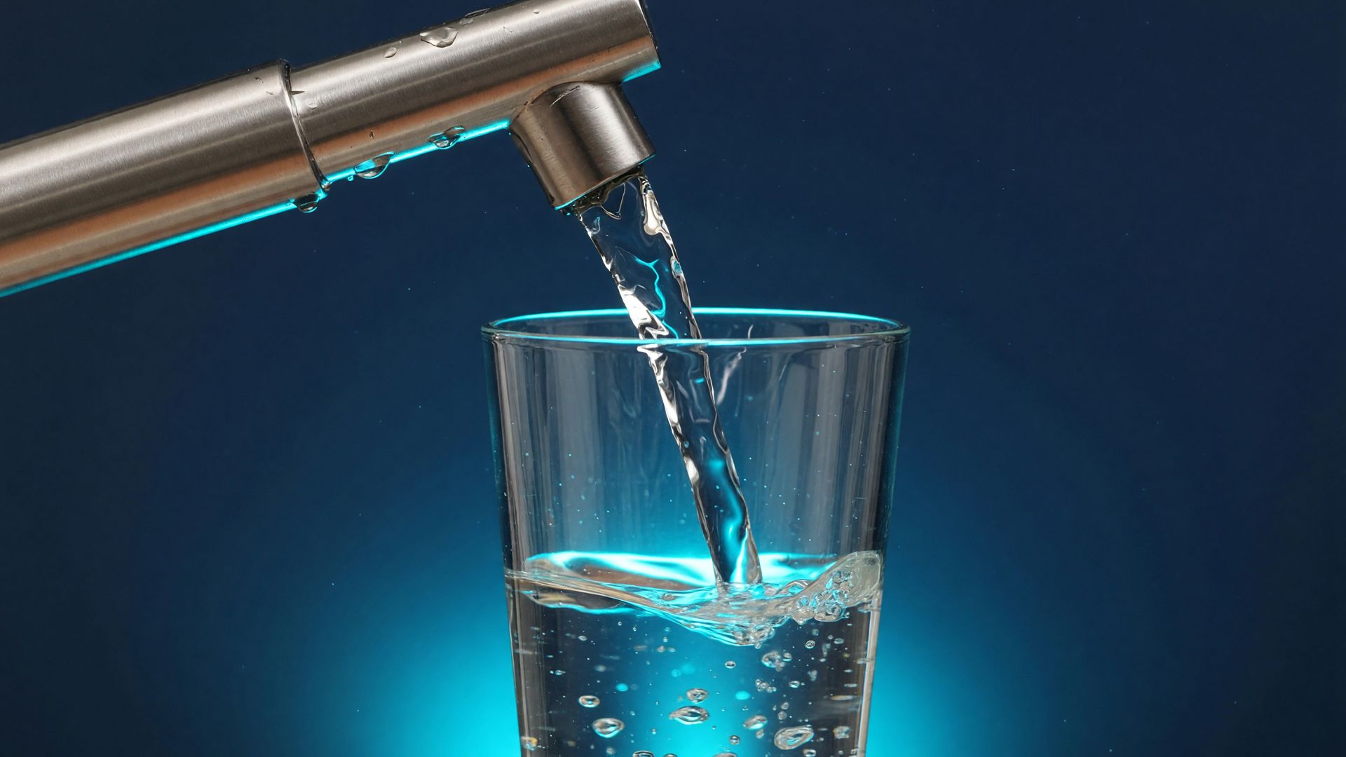 Klares Wasser fließt aus einem Edelstahlhahn in ein Glas