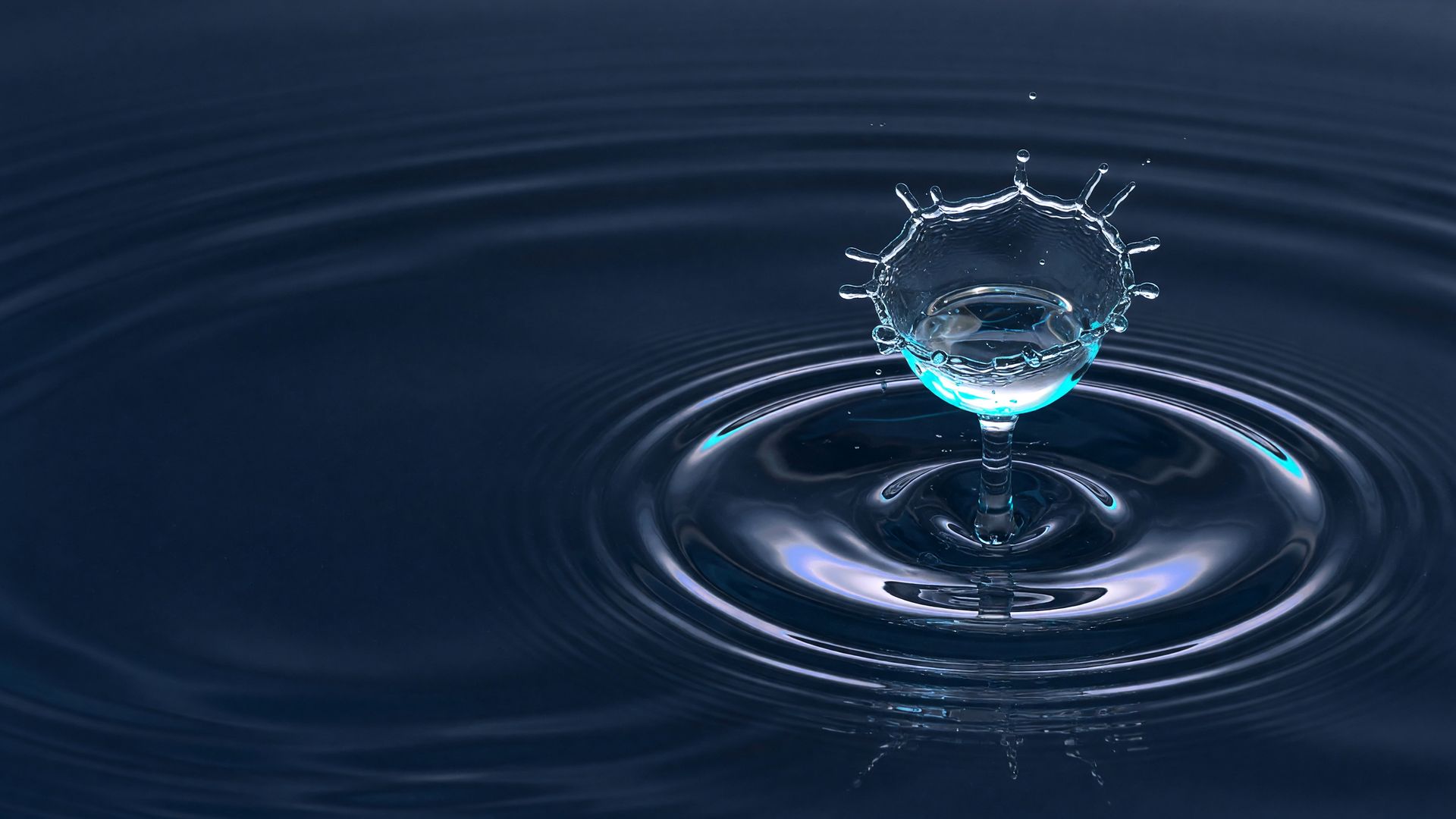 Wassertropfen fällt auf eine ruhige, dunkle Wasseroberfläche